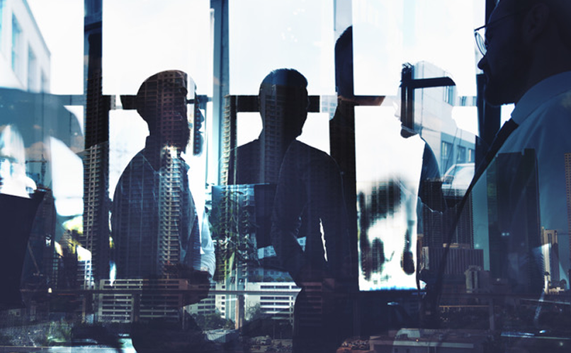 Sagome di persone d'affari in un ufficio con riflessi di edifici cittadini sulle vetrate.