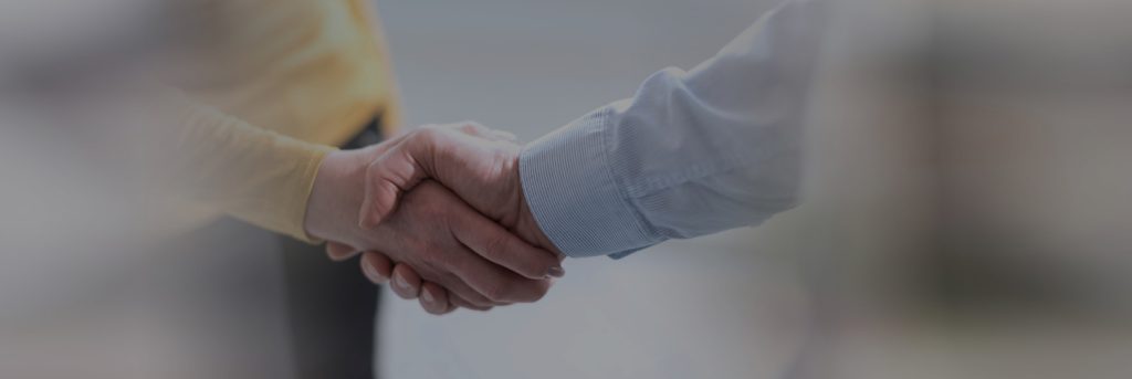 Stretta di mano tra due persone, una con camicia azzurra e l’altra con maglia gialla